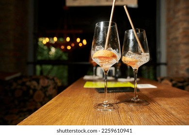 half-empty glasses with a cocktail, with ice and a slice of orange are on the table in the bar. Two half-empty glasses with ice and an orange slice stand on a table in a bar