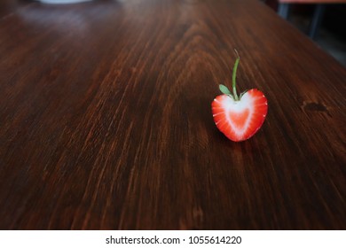A half-fresh, red strawberry placed on a wooden table