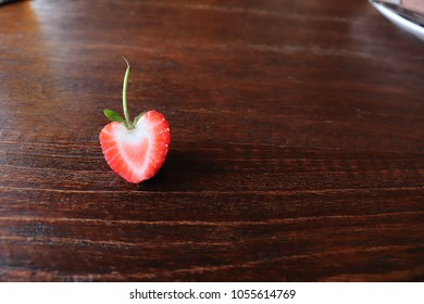 A half-fresh, red strawberry placed on a wooden table