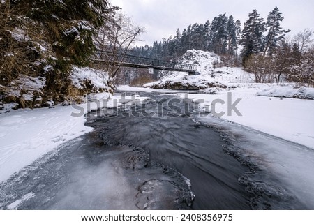 Half-frozen Hornad river with rapids in winter at sunset Slovak Paradise. An iron bridge over a frozen river. Discovering the beauty of the winter landscape.