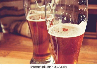 Half-full glasses of beer toned image. Glasses of beer on wooden table. Side view creative toned photo of man sitting at wooden table part view. There is free space in the left of table. A side-on view of multiple partially filled glasses of golden beer arranged in a line on a rustic wooden table, captured with a warm, color-toned treatment that enhances the amber hues and inviting foam. The varying levels in the glasses and the soft focus of the background create visual rhythm and depth, while the natural wood grain adds texture and an authentic pub-style atmosphere. This image conveys themes of social gatherings, casual drinking, craft beer culture, celebration, hospitality, and leisurely moments. Its rich colors, sharp detail in the liquid and glass surfaces, and smooth tonal grading make it ideal for editorial and commercial use in restaurant menus, beverage advertising, bar and brewery branding, lifestyle content, websites, posters, and social media campaigns.