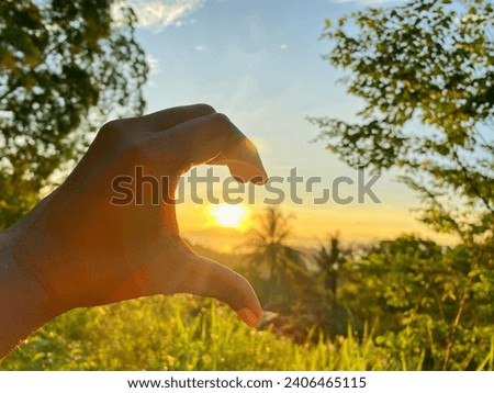 Half-hearted hands. The image shows the beautiful nature of Papua with half-heart-shaped hands against a background of sky, mountains, plants and the rising sun