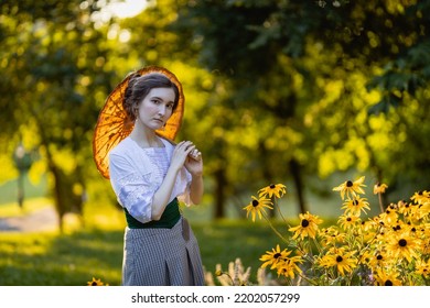 Half-lenght portrait of a young slender woman in a 1910s costume. Lady walking in the garden using an old-fashioned sun umbrella