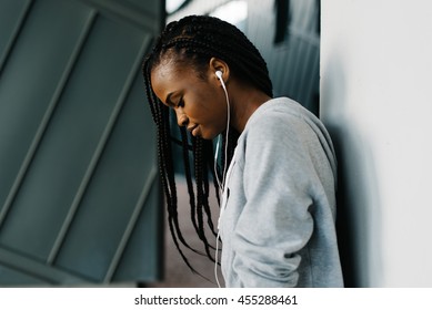 Half-length close-up portrait of excited young African girl wearing hoodie and cool earphones standing looking down