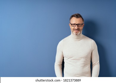 Half-length front portrait of a smiling handsome middle-aged man in white turtleneck against blue wall background with copy space