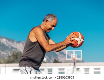 Half-length portrait of 60-years old smiling basketball player in good shape holding a sport ball outdoor - Shutterstock ID 2180103903