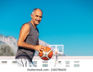 Half-length portrait of 60-years old smiling basketball player in good shape ready to shoot or pass a sport ball outdoor - Powered by Shutterstock