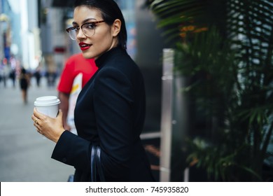 Half-length Portrait Of Attractive Confident Business Woman In Elegant Wear Strolling On Street In Downtown, Serious Female Executive Manager In Stylish Eyeglasses And Red Lips Looking At Camera 
