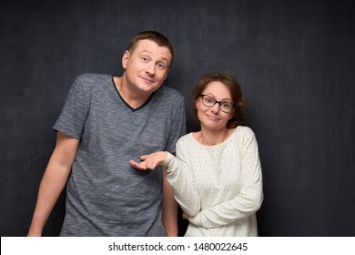 Half-length Portrait Of Confused Caucasian Couple Shrugging Their Shoulders Being Unsure And Doubting, Not Knowing What To Do Or How This Happened, Looking Uncertainly At Camera, Over Gray Background