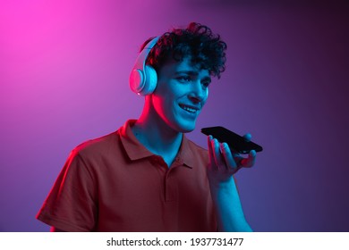 Half  length portrait man in headphones talking phone isolated over gradient pink  purple background in neon light  Concept human emotions  facial expression  youth culture  Copy space for ad 