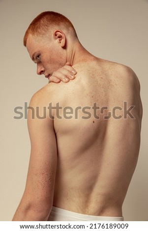 Half-length portrait of muscular male back isolated over grey studio background. Model posing in underwear. Masculinity. Concept of men's health, beauty, body and skin care, fitness. Body art