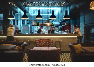 Half-lighted hall in a loft style in a mexican restaurant with open kitchen on the background. In front of the kitchen there are wooden tables with multi-colored chairs and sofas. On the sofas there - Shutterstock ID 430097278