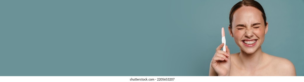 Half-naked Ginger Woman Smiling And Showing Pregnancy Test Isolated Over Blue Background