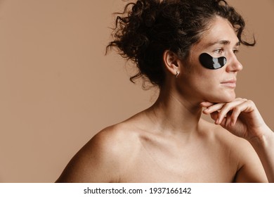 Half-naked woman looking aside while posing with eye patches isolated over beige background