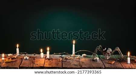 Halloween background. Scary black spider, candles and leaves on wooden planks table with night neon backdrop. 