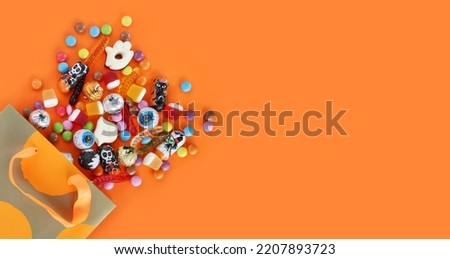 Halloween banner with shopping paper orange polka dot gift bag in corner full of assorted traditional candies. Orange background with copy space. Happy Halloween holiday sale, trick or treat concept.