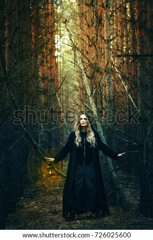 Halloween. beautiful girl with a lantern in a black dress in the forest