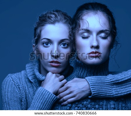 Halloween beauty portrait of two young women in gray sweaters on grey studio background. Beautiful girls stretching hands forward in embrace. Female friendship concept. One girl with eyes closed.