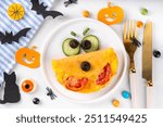 Halloween breakfast eggs omelet shaped and decorated like cute monster, with fresh vegetables, funny kids Halloween food simple recipe idea