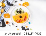 Halloween breakfast eggs omelet shaped and decorated like cute monster, with fresh vegetables, funny kids Halloween food simple recipe idea