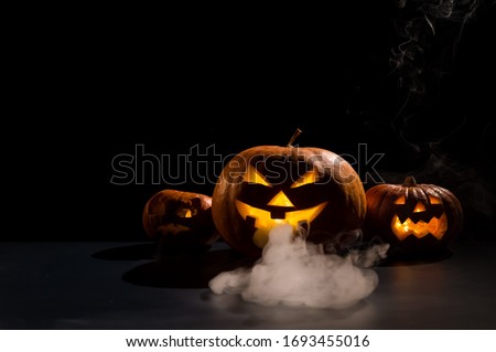 Halloween card. jack o lantern with candles glow on a black background. A row of creepy pumpkins with carved grimaces smokes in the dark.