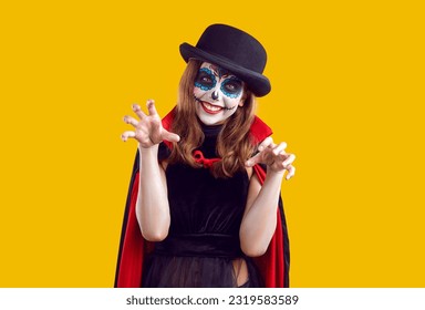 Halloween and childhood. Funny preteen girl playfully scares you by attacking and scratching during Halloween fun. Creative smiling child in Halloween costume makes claw gesture on orange background.