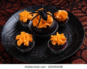 Halloween Chocolate Cupcake With Orange Frosting And A Spider On Top With Four Mini Cupcakes Sitting On A Black Spiderweb Plate