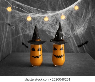 Halloween cocktail glasses with jack lantern face in black witch hats on a gray background with cobwebs. Serving for Halloween party. - Powered by Shutterstock