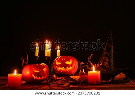 Halloween composition with jack-o-lanterns, witch hat and burning candles on wooden table
