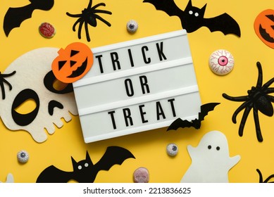 Halloween Concept Background. Top View Of Light Box With The Text Trick Or Treat And Halloween Decoration Over Yellow Background