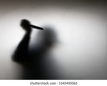 Halloween concept. Blurred shadow of hand holding sharp knife behind white mirror background.  Murder scene.