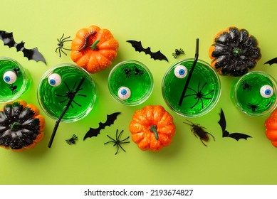 Halloween concept. Top view photo of green floating eyeball punch in glasses spiders bat silhouettes pumpkins spooky insects cockroach and centipede on isolated light green background