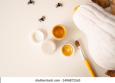 Halloween Concept. White And Gold Painted Pumpkin On The Table Decorated With Spiders, Paints And Autumn Leaves. Halloween Crafts