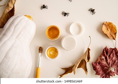 Halloween Concept. White And Gold Painted Pumpkin On The Table Decorated With Spiders, Paints And Autumn Leaves. Halloween Crafts