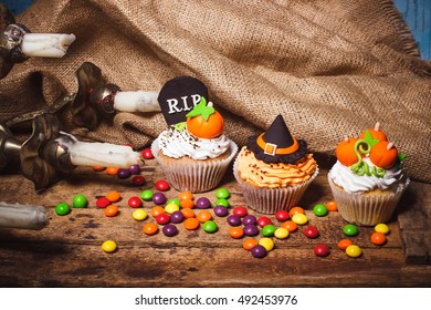 Halloween cupcakes with colored decorations: tombstone, witch hat and pumpkins made from confectionery mastic, soft focus background