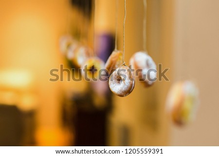 Halloween decoration.  Doughnuts hanging on strings. Children's game. Blurred bokeh background. Yellow, creme, beige. Diminishing perspective. Small sweets. Trick or treat. Sugar.