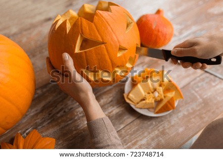 halloween, decoration and holidays concept - close up of woman with knife carving pumpkin or jack-o-lantern at home
