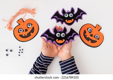 Halloween Decorations In Child Hands Over White Table. Halloween Preparation, Kids Craft Concept. Top View.