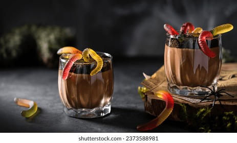 Halloween dessert for party - delicious chocolate mousse with chocolate cookie crumbs and gummy worms in glasses on a table with festive halloween decorations. Close up. Recipe, menu - Powered by Shutterstock