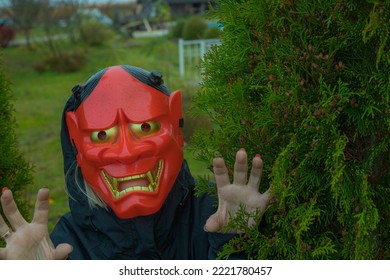 Halloween Devil Mask For A Woman, A Woman Behind A Bush Near A House In A Garden. A Festive Event. Zina, Latvia - 02.11.2022