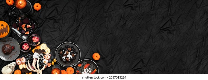 Halloween Dinner Party Corner Border Over A Dark Black Banner Background. Overhead View. Charcuterie Board, Black Risotto And Pasta, Spider Cake, Jack O Lantern Pumpkin Soup And Apple Skull Wine