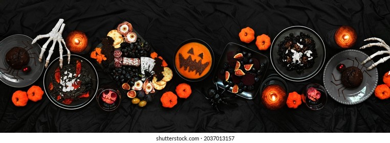 Halloween Dinner Party Table Scene Over A Dark Black Banner Background. Above View. Spooky Charcuterie Board, Black Risotto And Pasta, Spider Cakes, Jack O Lantern Pumpkin Soup And Apple Skull Wine