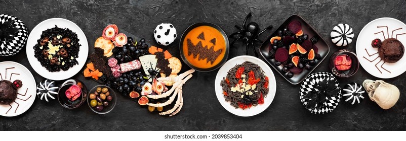 Halloween Dinner Party Table Scene Over A Black Banner Background. Above View. Spooky Charcuterie Board, Black Risotto And Pasta, Spider Cakes, Jack O Lantern Pumpkin Soup, Salad And Apple Skull Wine.