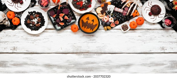 Halloween Dinner Party Top Border Over A White Wood Banner Background. Overhead View. Black Risotto And Pasta, Charcuterie Board, Jack O Lantern Pumpkin Soup, Spider Cakes, And Apple Skull Wine.