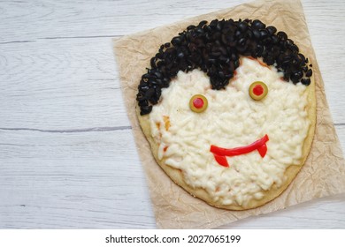 Halloween Dracula Pizza Made From Pizza Dough,pizza Sauce,mozzarella Cheeses,black Olives,green Olives And Red Bell Peppers On Parchment Paper With Wooden Background.Art Food Idea For Kids Party