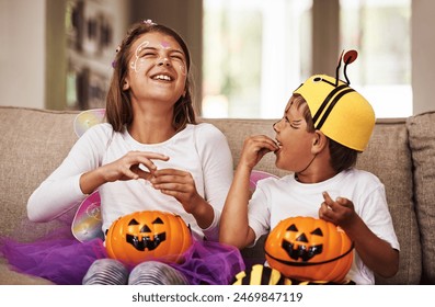 Halloween, eating candy and kids in home with costume for holiday event, celebration and happiness with pumpkin. Couch, young girl and boy with orange vegetable for sweets, smile and fairy outfit - Powered by Shutterstock