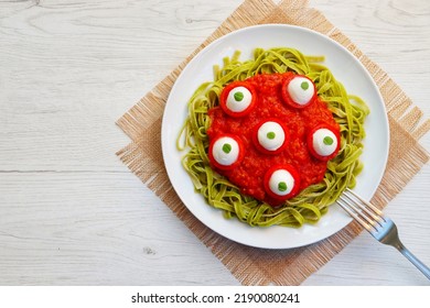 Halloween eyeballs pasta-spinach fettuccine pasta with tomato sauce,mozzarella balls,cherry tomatoes and basil on plate with white wood background.Creative food idea for Halloween's dinner.Top view