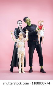 Halloween Family. Happy Father, Mother And Children Girls In Halloween Costume And Makeup. Bloody Theme: The Crazy Maniak Faces On Pink Studio Background