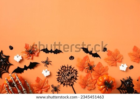 Halloween flat lay composition with pumpkins, skeleton hands, spiders, bats, maple leaves on orange background. Happy Halloween banner design.