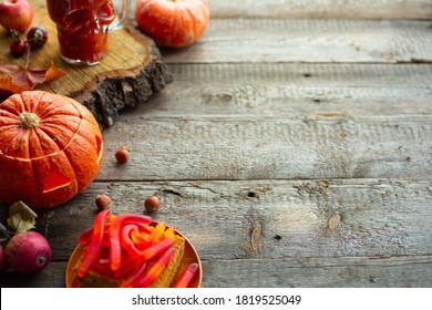 Halloween Food Still Life Abstract Background With Pumpkins, Apples, Cake, Gummy Worms, Skull Red Drink And Candles